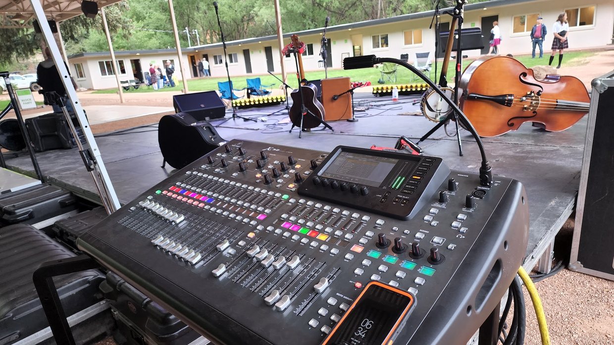 Digital mixing console at front of house for an outdoor stage with acoustic instruments