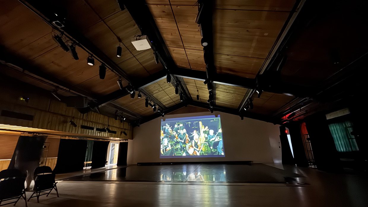 Timber-framed performance hall with track lighting, projector and projection screen in use