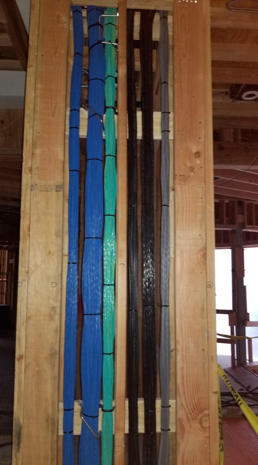 Category, coax and control cable bundles dressed vertically in a stud bay before drywall